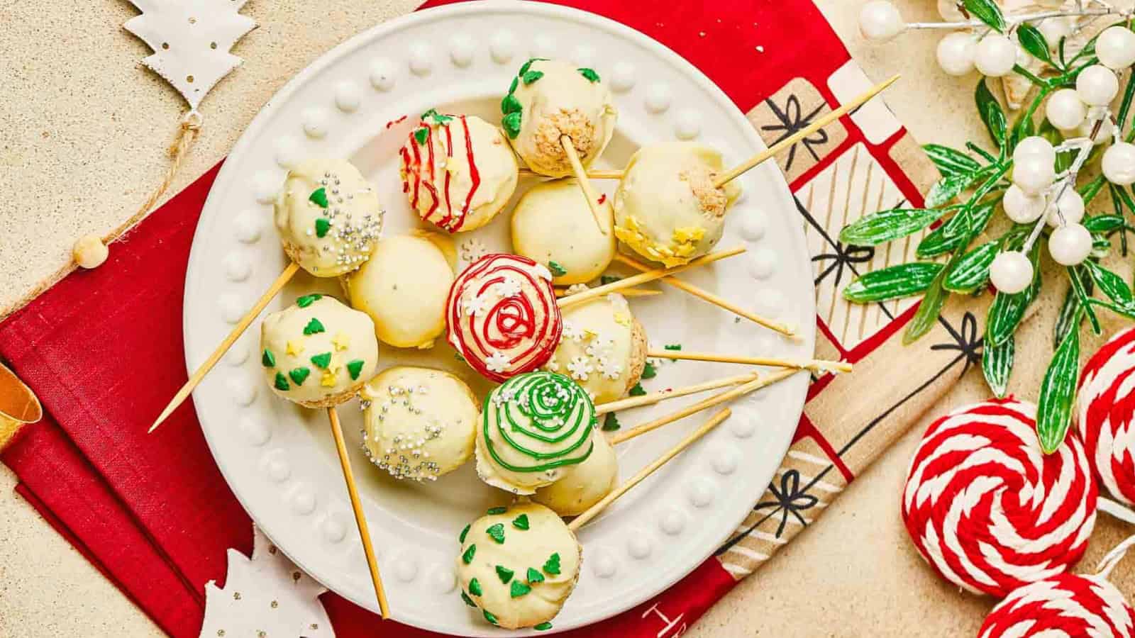 A plate of decorated holiday cake pops on sticks, with red, green, and white frosting and sprinkles.