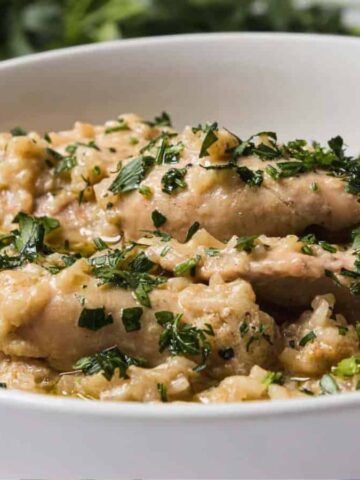 A bowl of creamy chicken stew garnished with chopped herbs and served with a spoon.