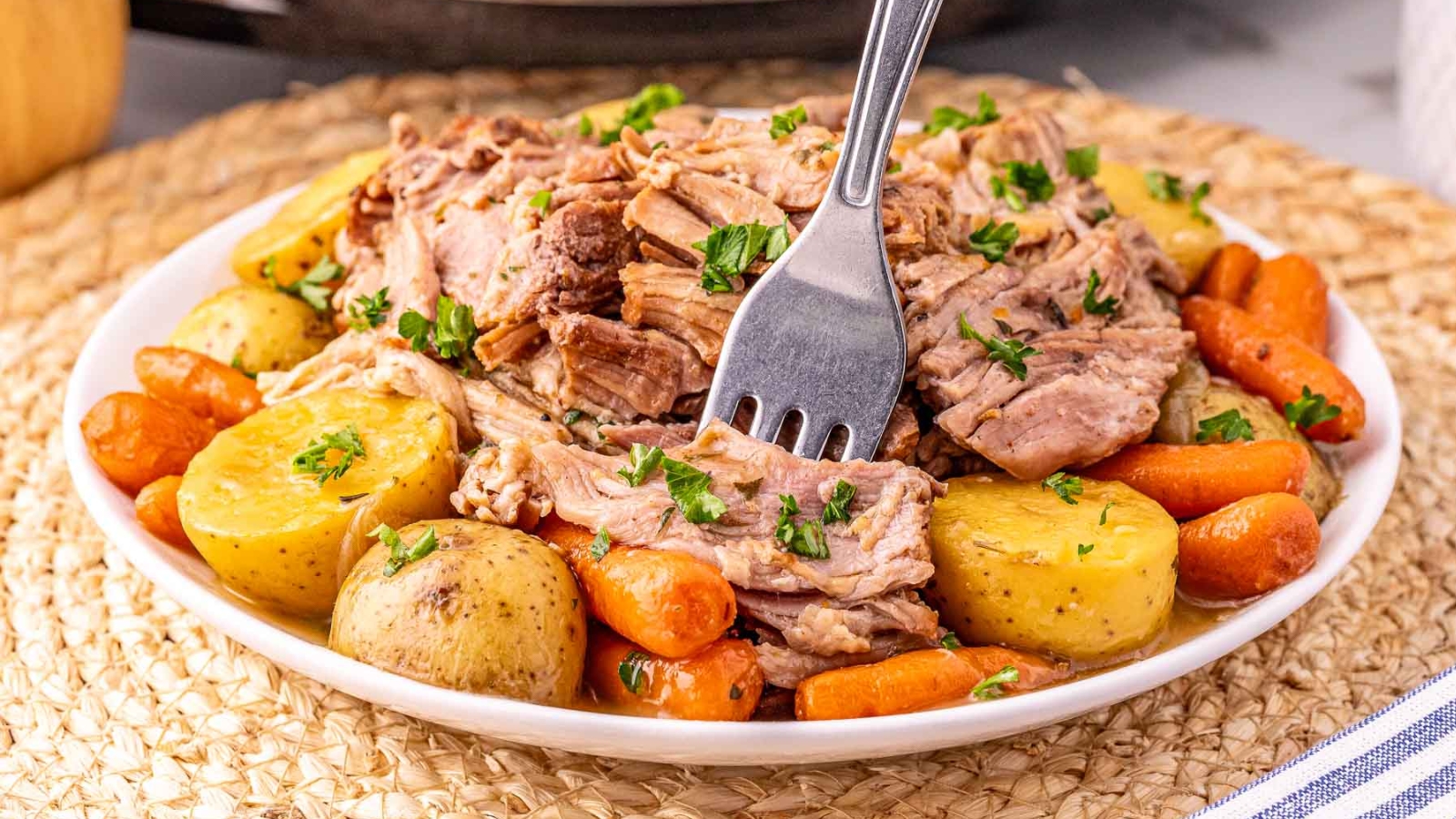 A bowl of shredded pot roast with baby potatoes and carrots, garnished with parsley, on a woven placemat.