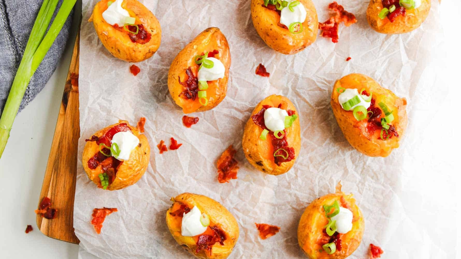 Mini baked potatoes topped with sour cream, bacon bits, cheddar cheese, and chopped green onions.