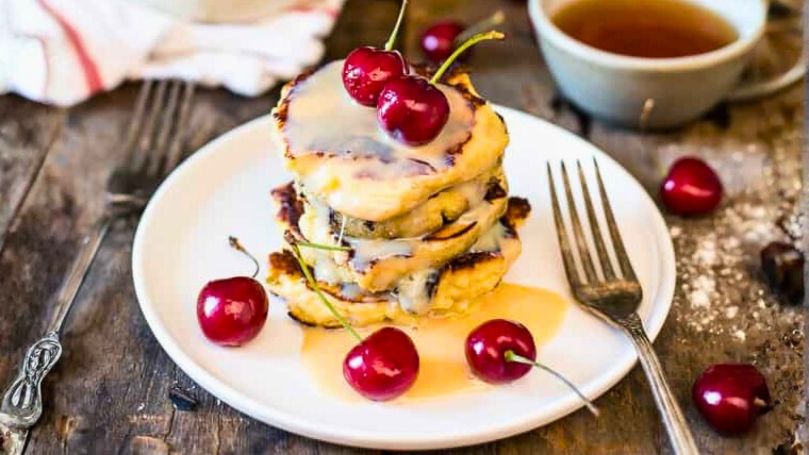 Stack of Russian cottage cheese pancakes topped with cherries and cream sauce.