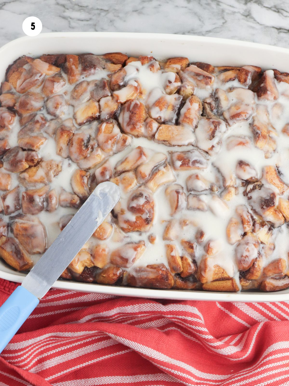 baked casserole in dish with cinnamon roll icing spread on top.