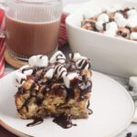 piece of Pillsbury Hot Cocoa Cinnamon Roll Breakfast Casserole on plate with chocolate syrup on top.