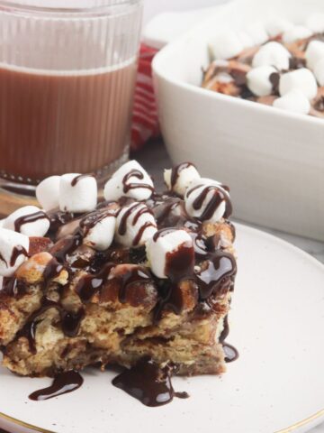 piece of Pillsbury Hot Cocoa Cinnamon Roll Breakfast Casserole on plate with chocolate syrup on top.