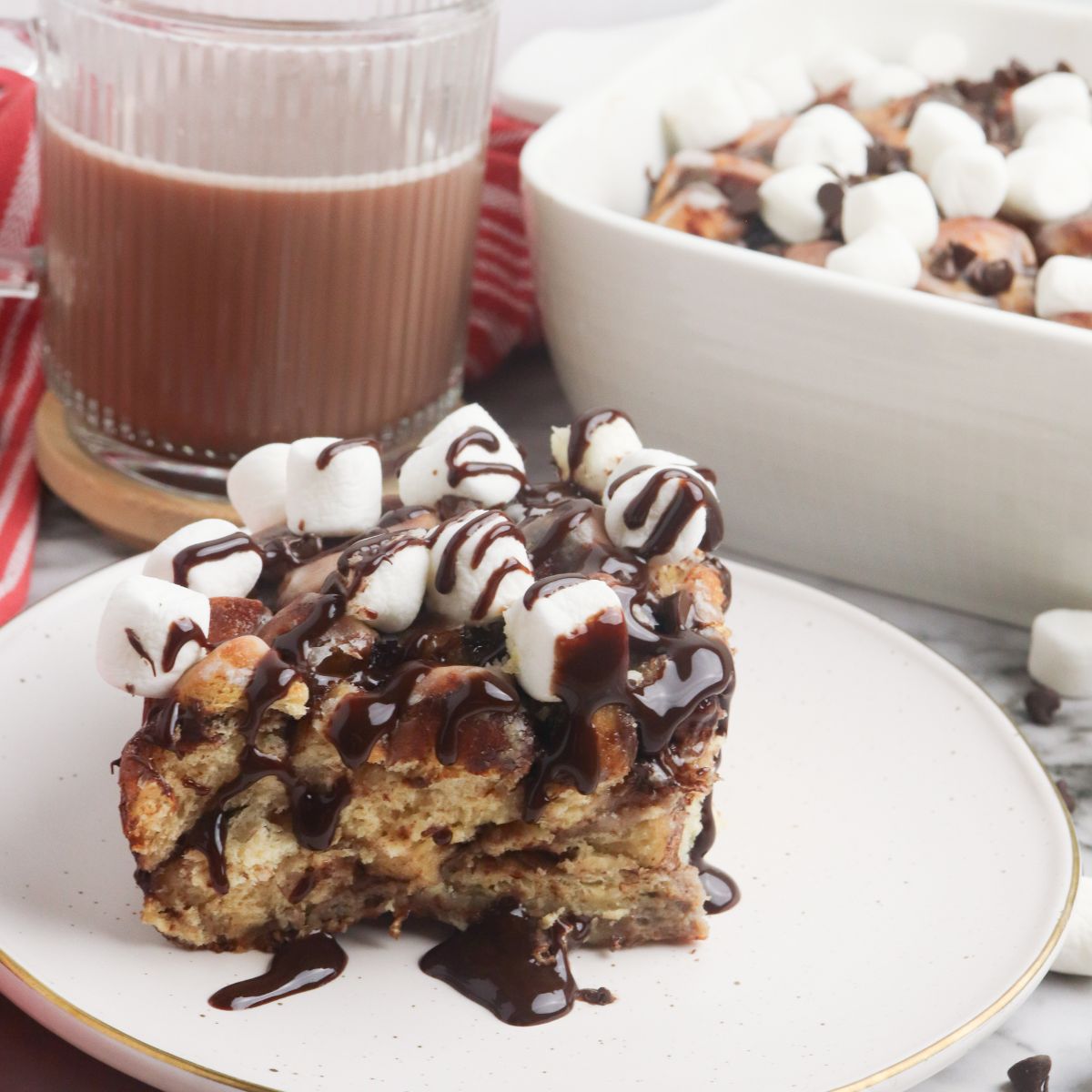 piece of Pillsbury Hot Cocoa Cinnamon Roll Breakfast Casserole on plate with chocolate syrup on top.