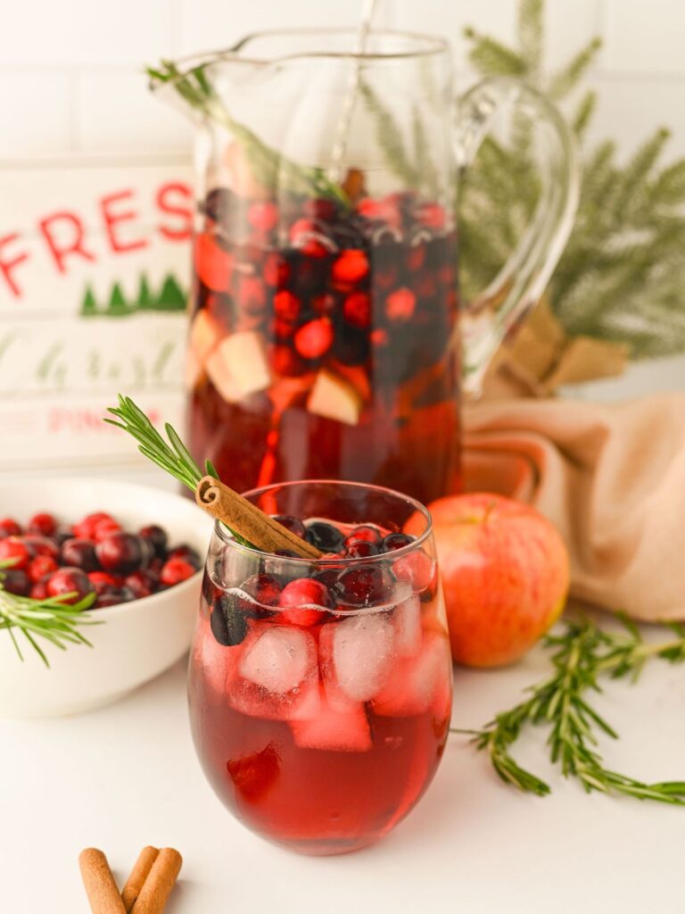 Glass of Cranberry Apple Punch with the pitcher of the rest of the punch in the background.