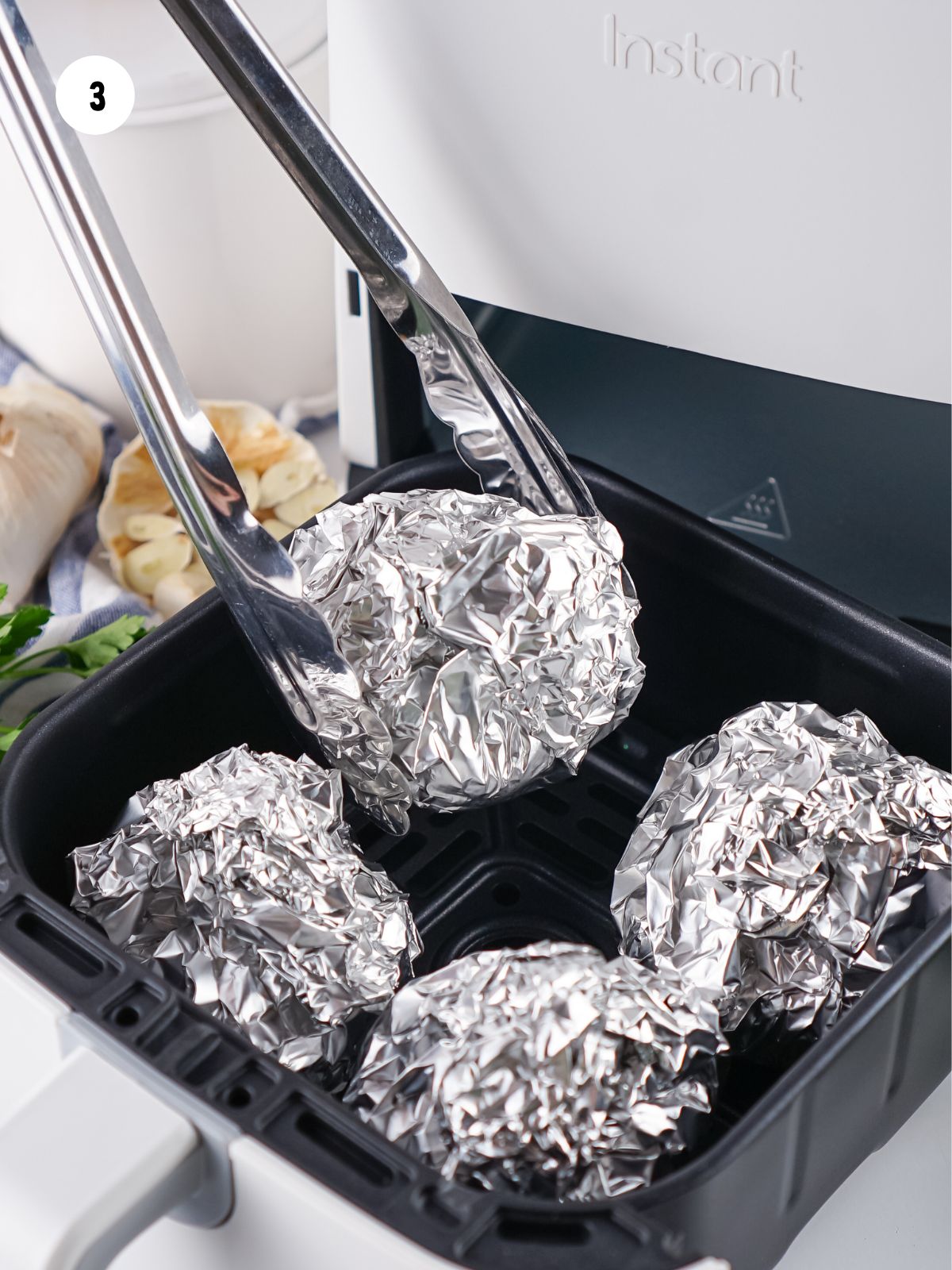 Garlic bulbs wrapped in foil and placed in the air fryer.