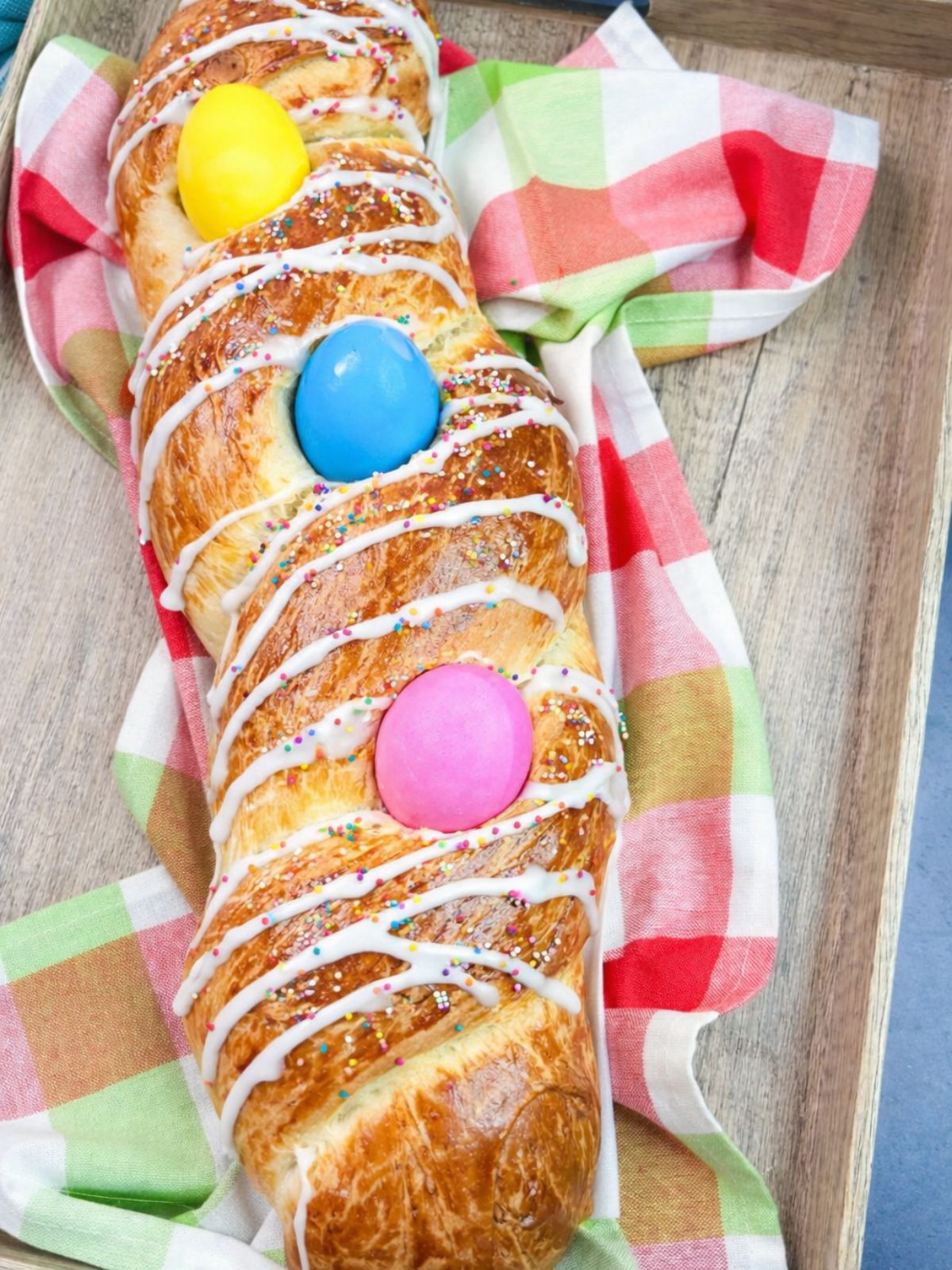 3 colored Easter eggs inside loaf of braided bread with icing.