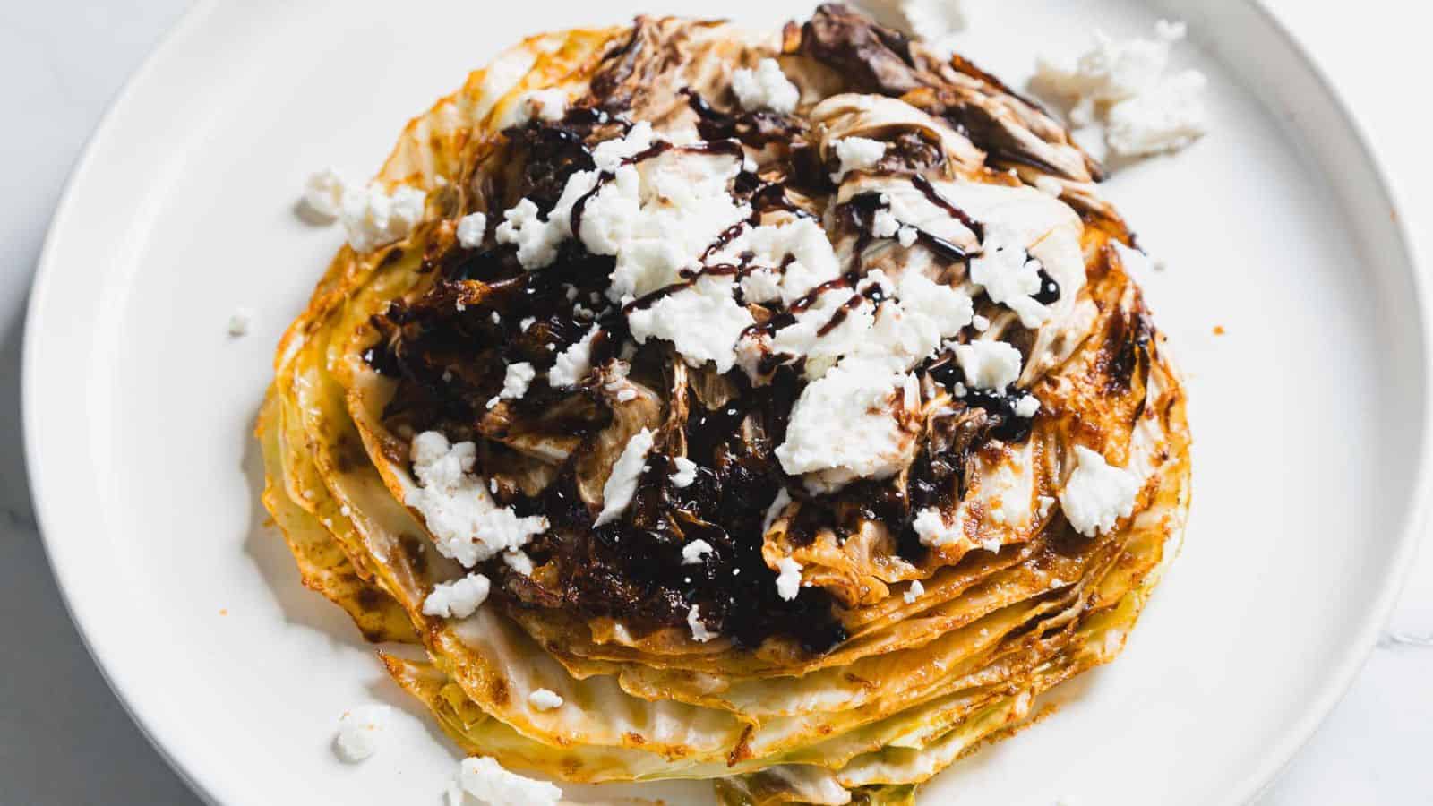 A stack of crepes topped with crumbled feta cheese and drizzled with balsamic glaze, served on a white plate.
