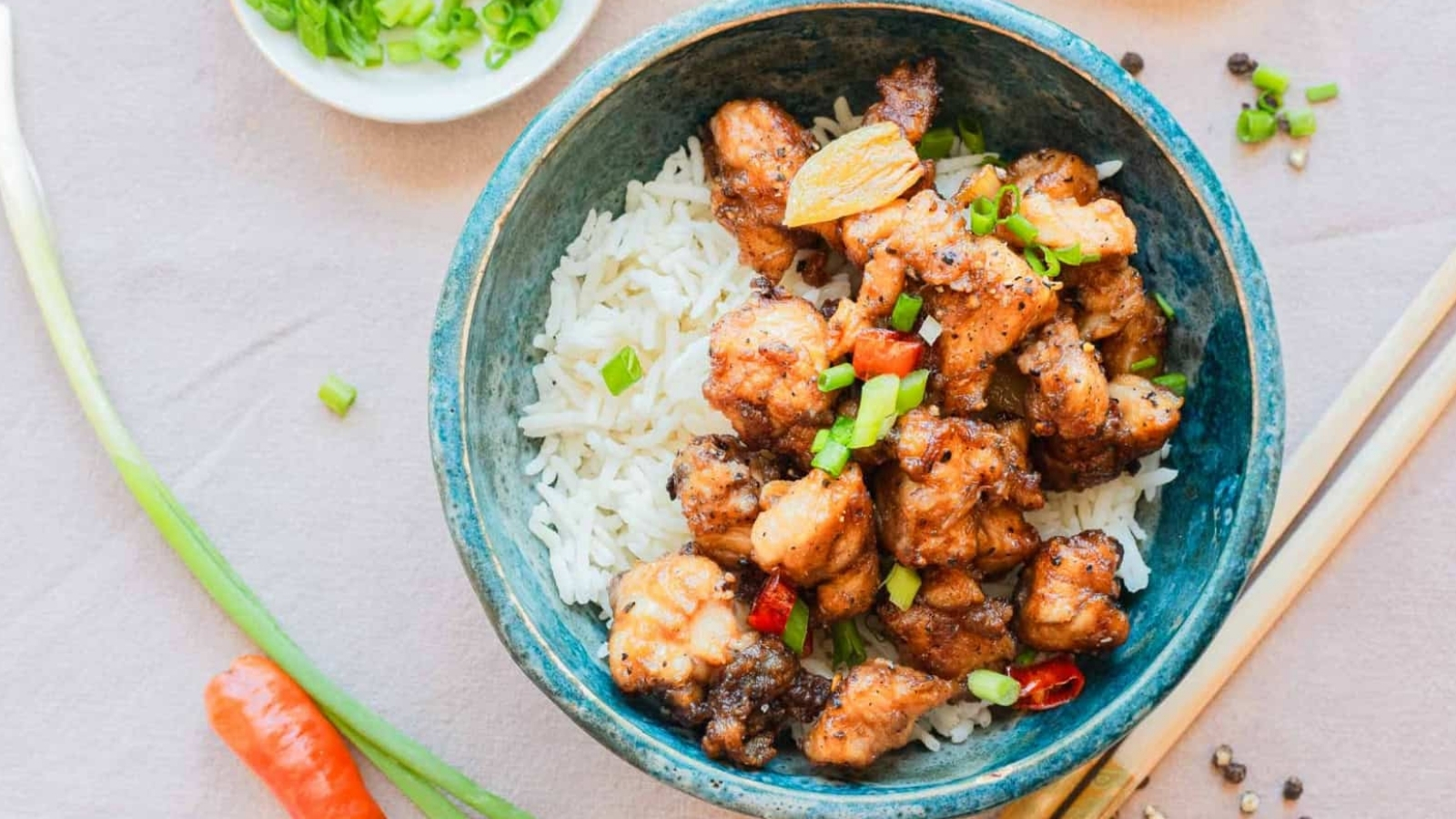A bowl of white rice topped with stir-fried chicken pieces and chopped green onions, with chopsticks beside it.