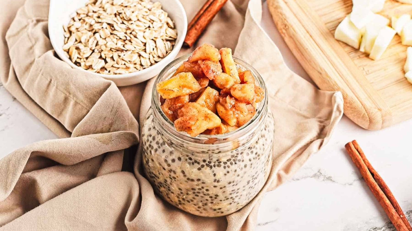 A jar of chia seed pudding topped with caramelized apple pieces, with apples in the background.