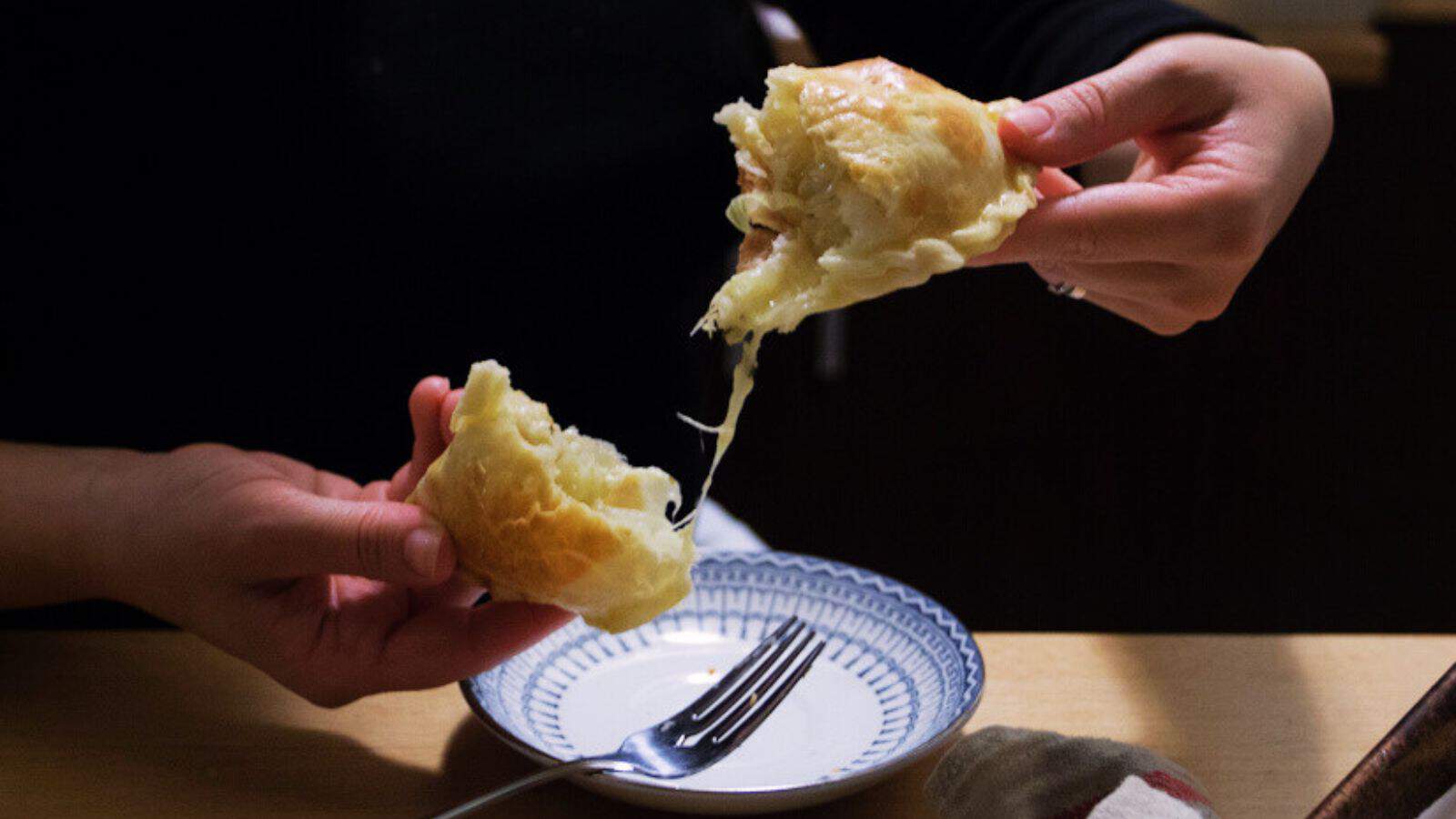 Argentinian empanada being pulled apart over a plate.