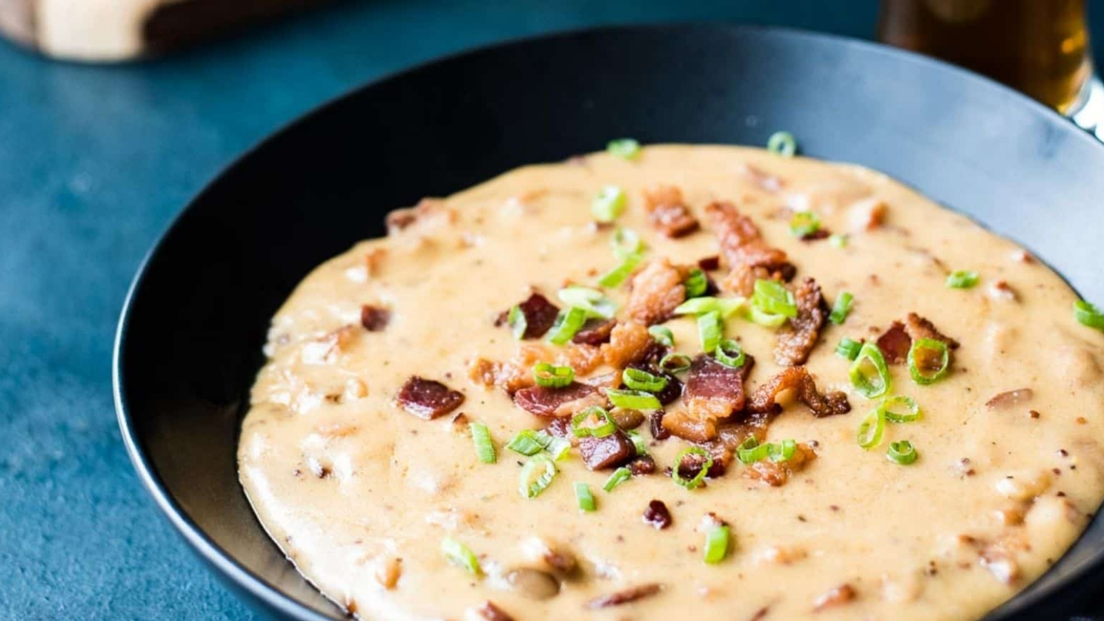 Bacon beer cheese in a dark bowl surrounded by pretzel knots on a cutting board.