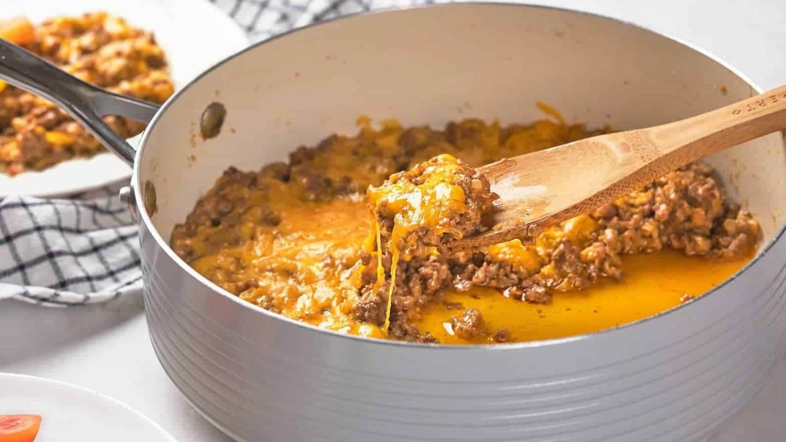 A wooden spoon scoops a portion of cooked ground meat with melted cheese from a pan.