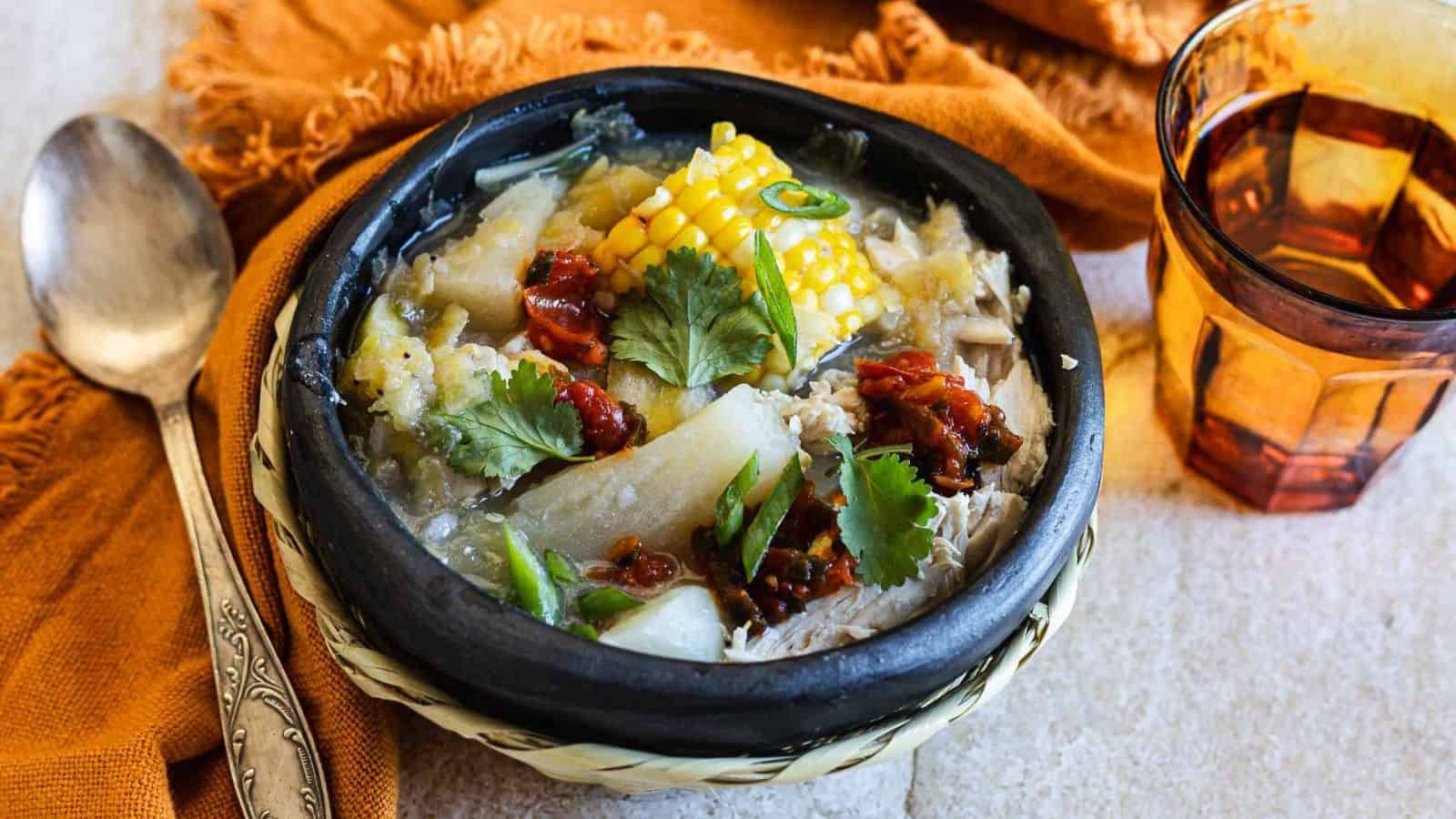 Bowl of chicken sancocho with corn, plantains, potatoes, and carrots in broth.