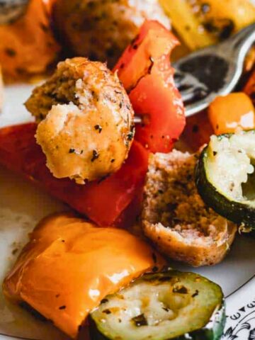 Close-up of roasted meatballs with a mix of colorful, chopped bell peppers and zucchini slices.