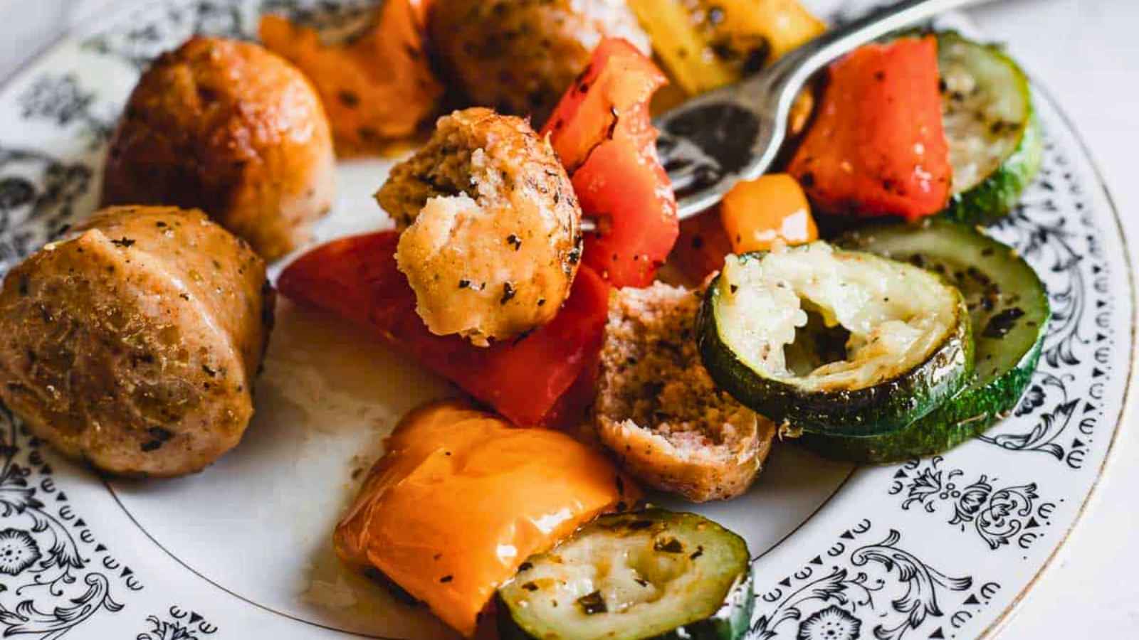 Close-up of roasted meatballs with a mix of colorful, chopped bell peppers and zucchini slices.