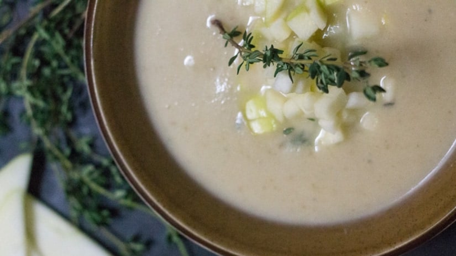 A bowl of soup with apples and sprigs of thyme.
