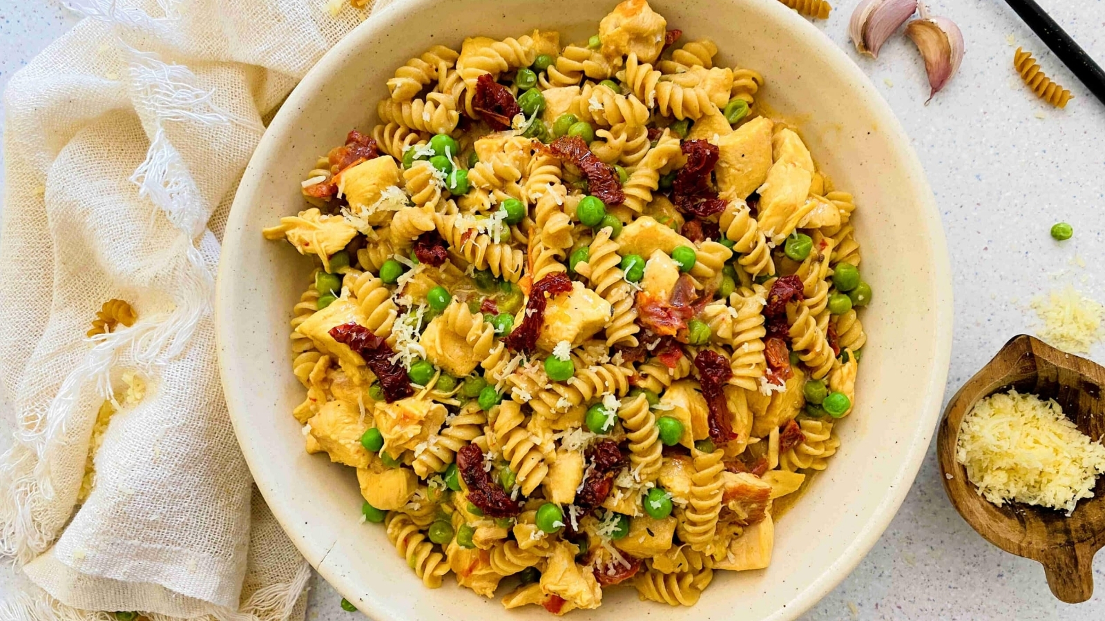 white bowl with chicken pasta with sundried tomatoes and peas and garlic and a light linen around the bowl.