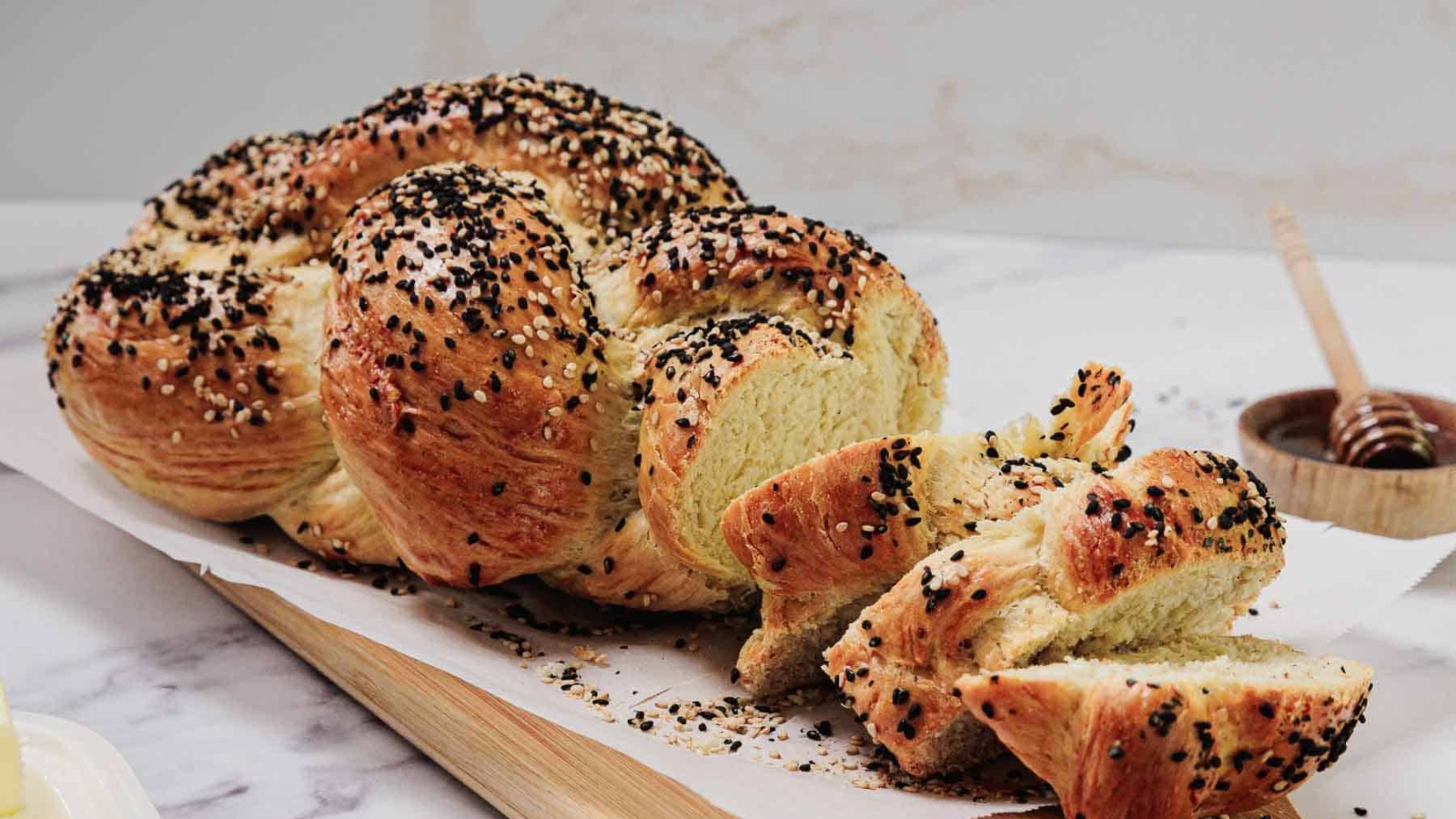 A braided loaf of seeded bread, partially sliced, on a wooden board.