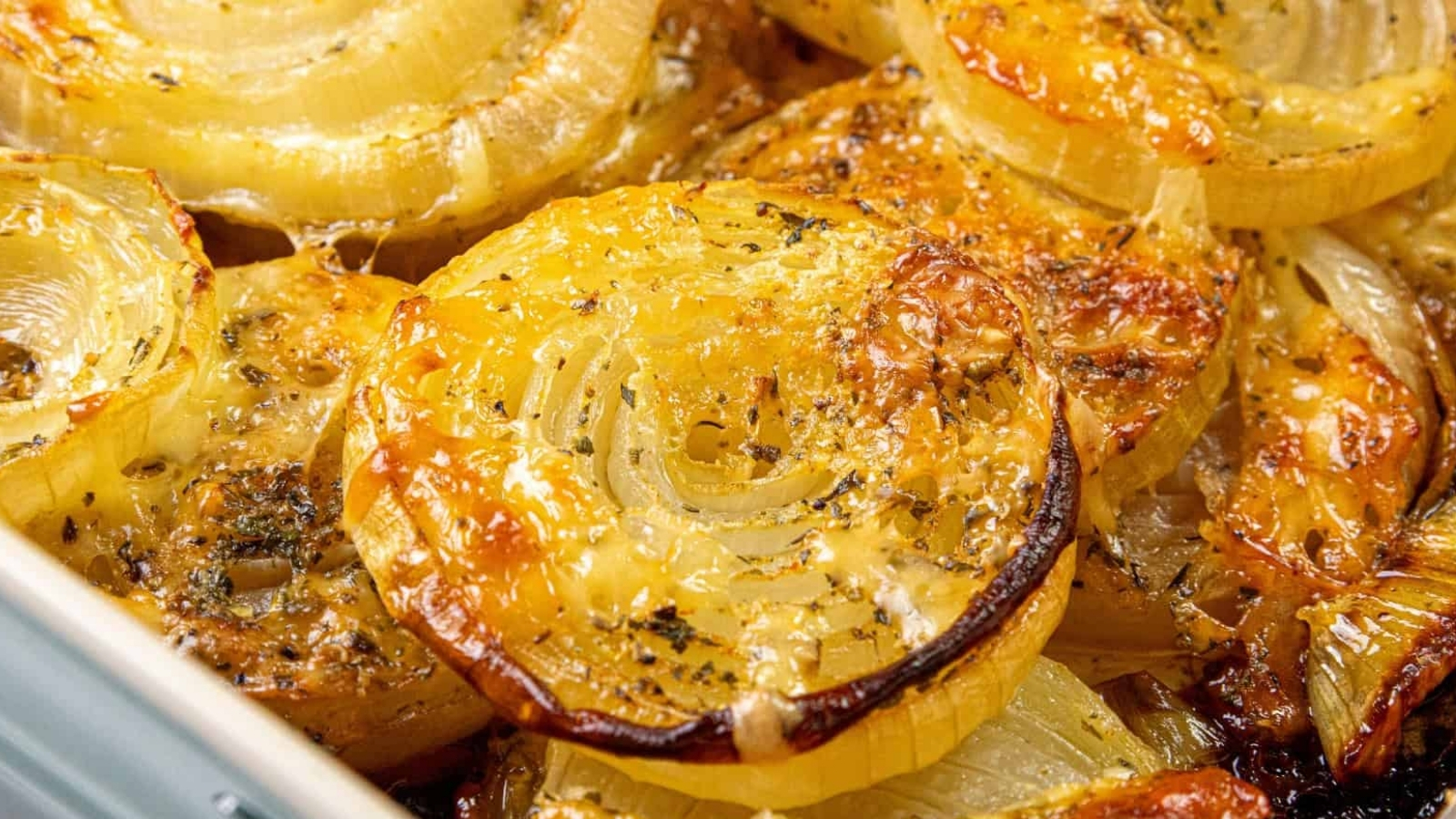 Close-up of roasted onion slices, golden and caramelized, sprinkled with herbs and seasoning.