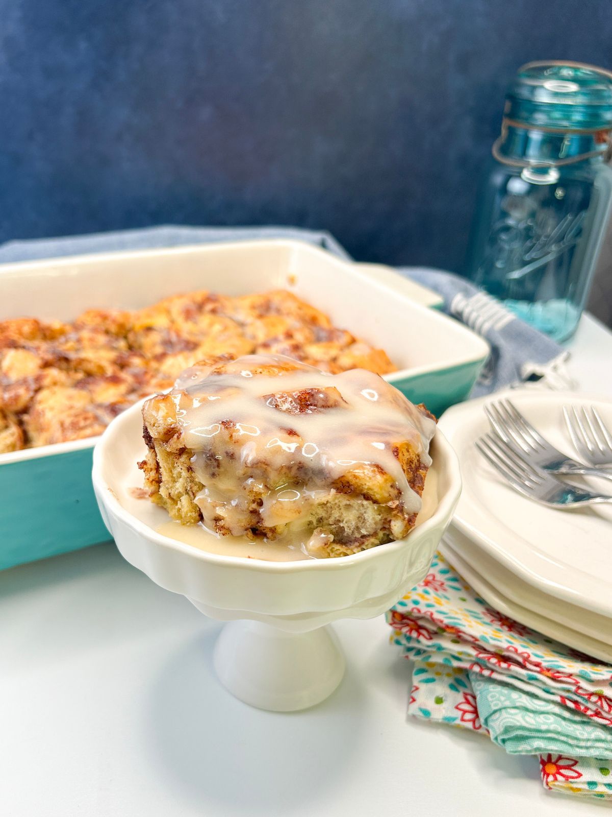 Cinnamon Roll Breakfast Casserole made with Refrigerated Cinnamon Rolls from Walking on Sunshine Recipes. baked cinnamon roll casserole in small dish with napkins, plates and forks.