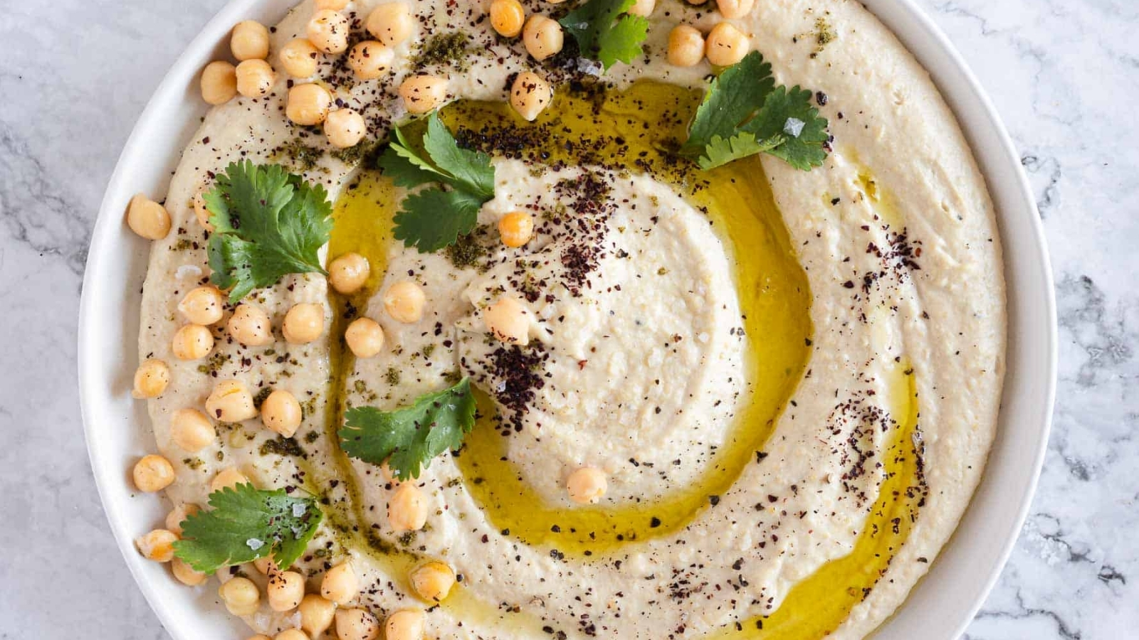 Garlic hummus on plate with parsley, zaatar and olive oil.