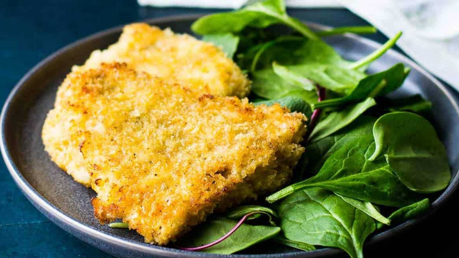 Panko crusted rockfish on a plate with spinach.