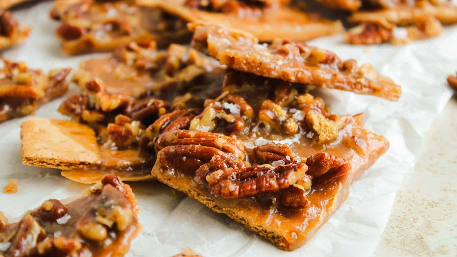 Close-up of pecan pie bark with caramelized pecans on top of graham crackers, arranged on parchment paper.