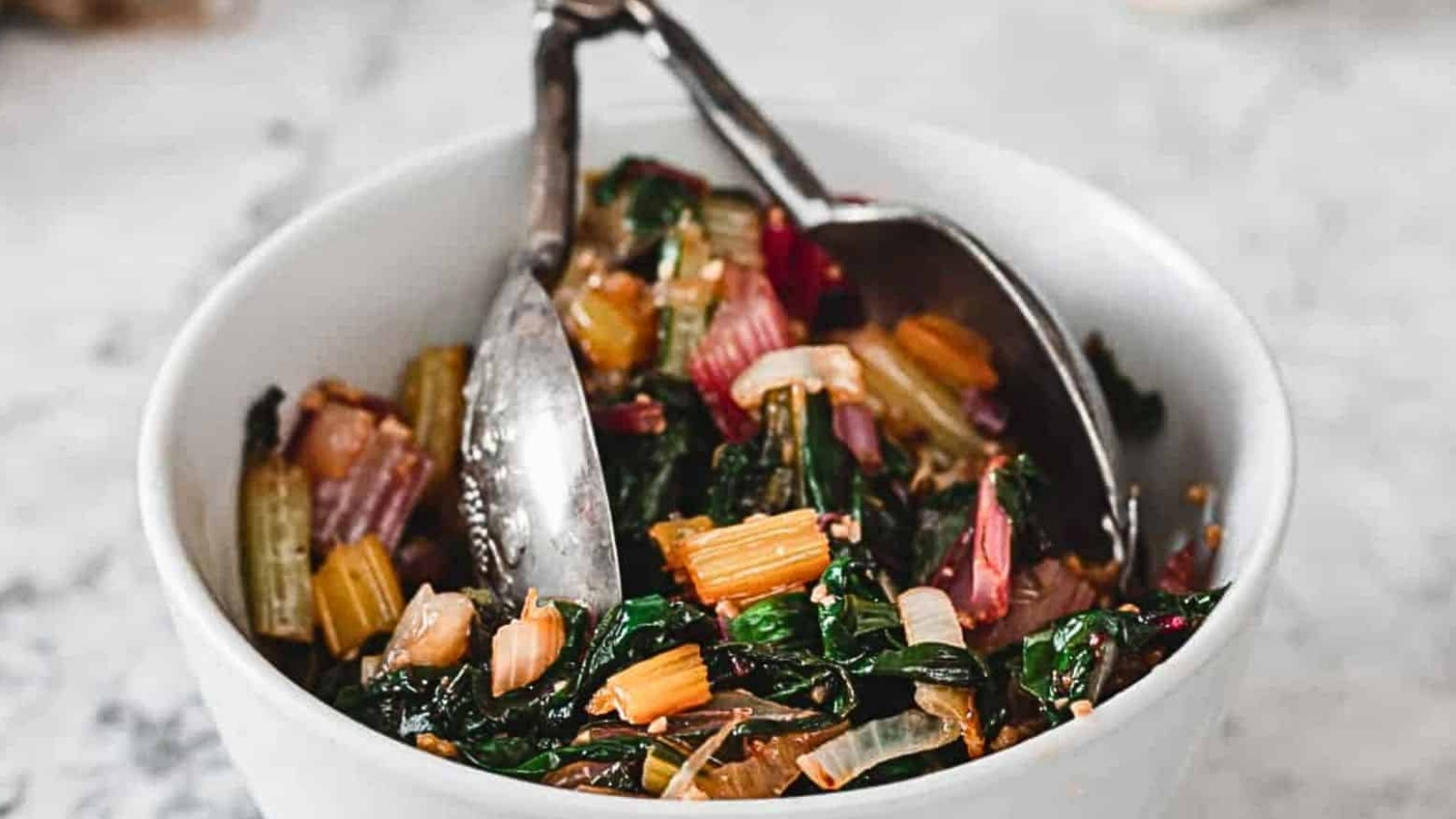 Side view of white bean salad in bowl with tongs.