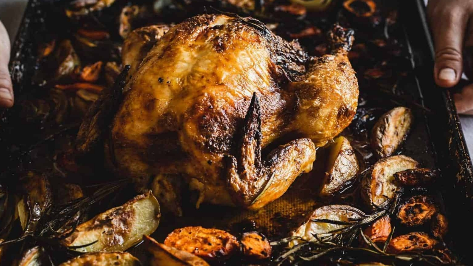 Hands holding paprika chicken and vegetables on a sheet pan.