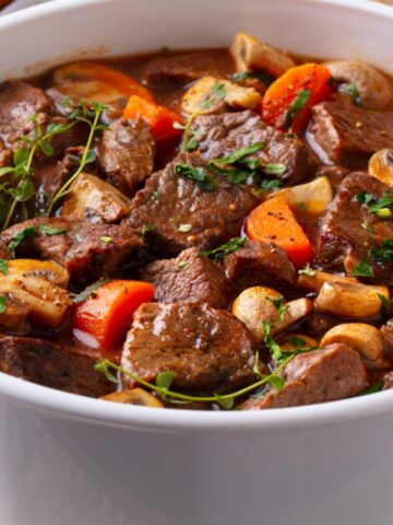 Beef stew in a white pot served with a spoon.