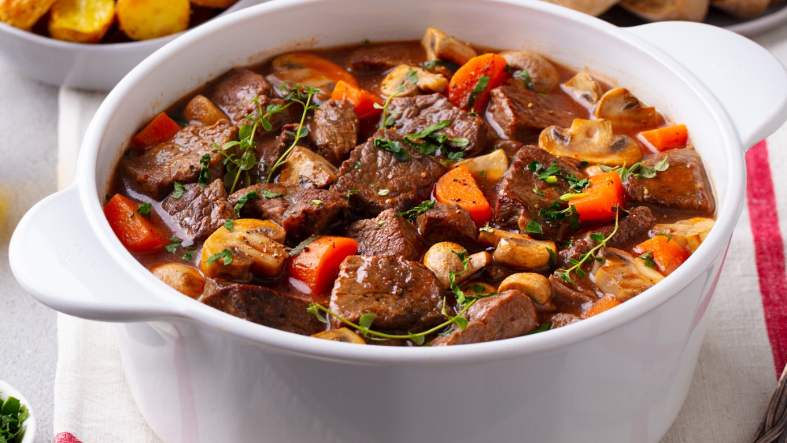 Beef stew in a white pot served with a spoon.