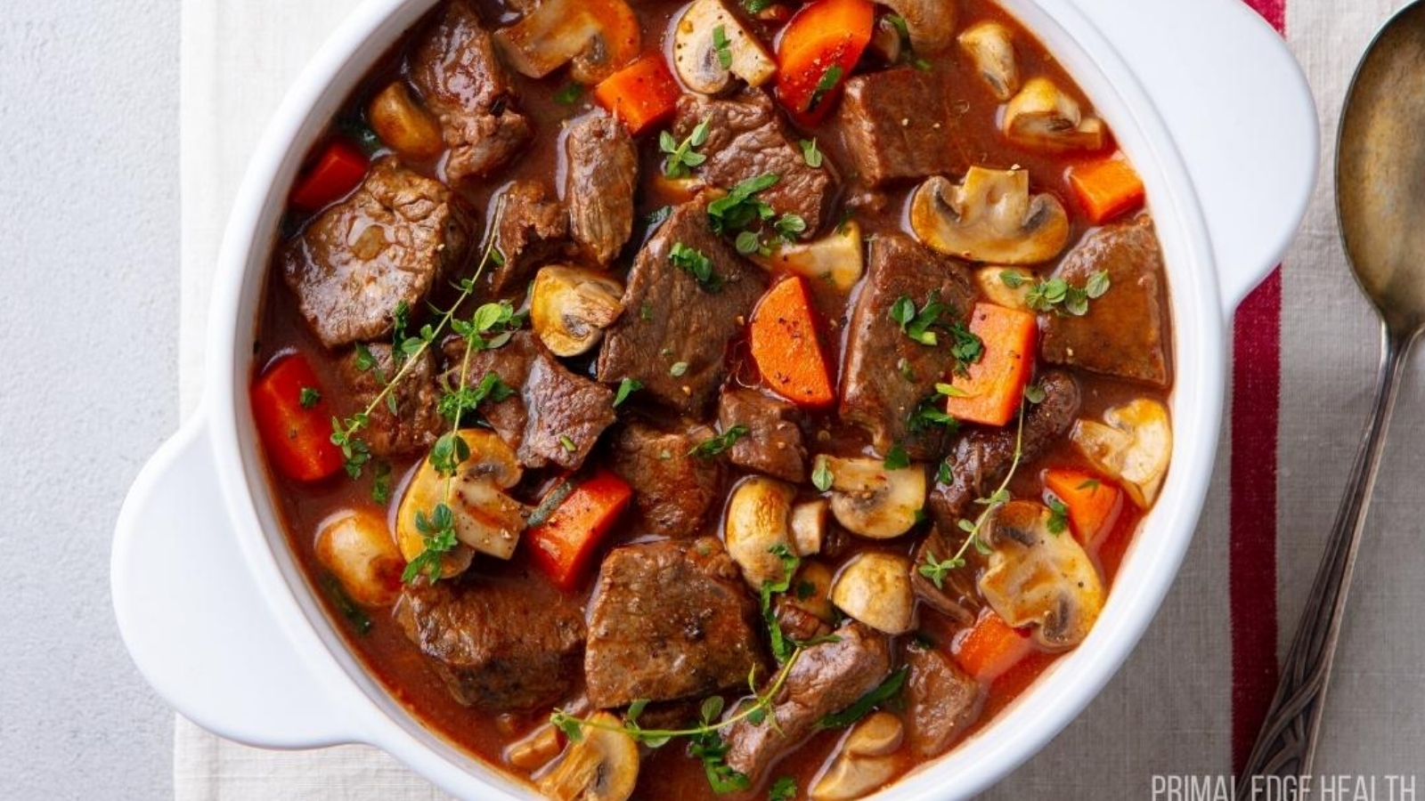 Beef stew in a white pot served with a spoon.