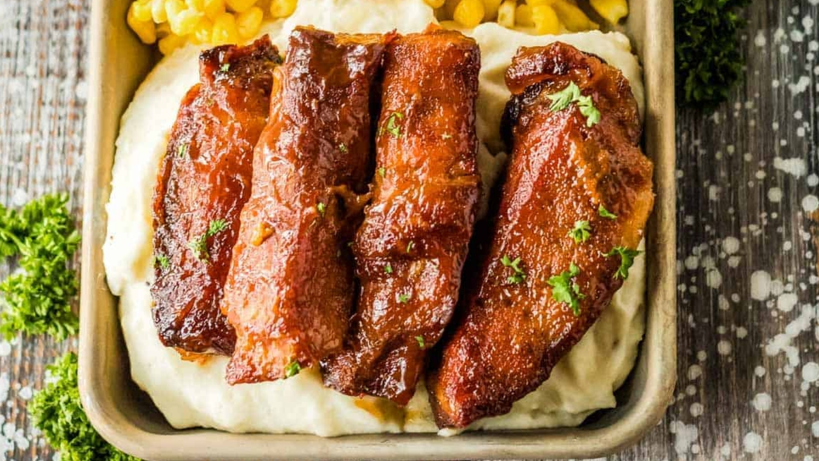 Slow cooker country style ribs on a tray on top of mashed potatoes with corn.