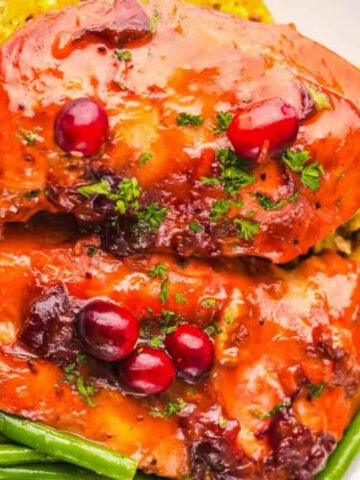 Glazed chicken breasts with cranberries, green beans, and stuffing on a white plate, garnished with parsley.