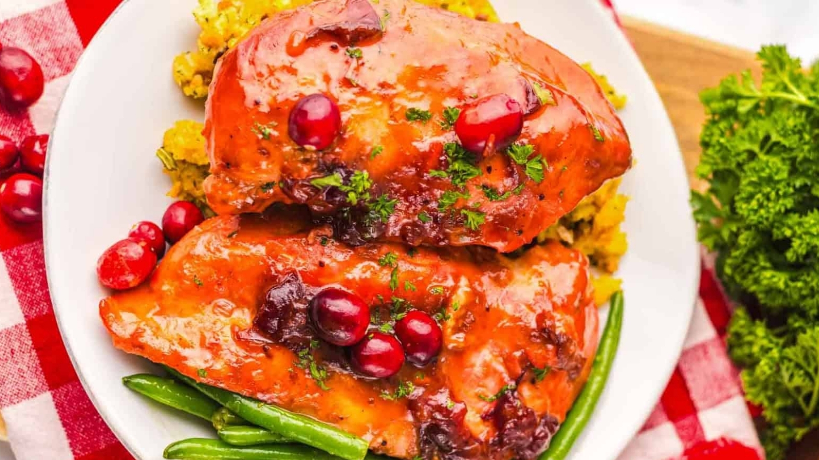 Glazed chicken breasts with cranberries, green beans, and stuffing on a white plate, garnished with parsley.