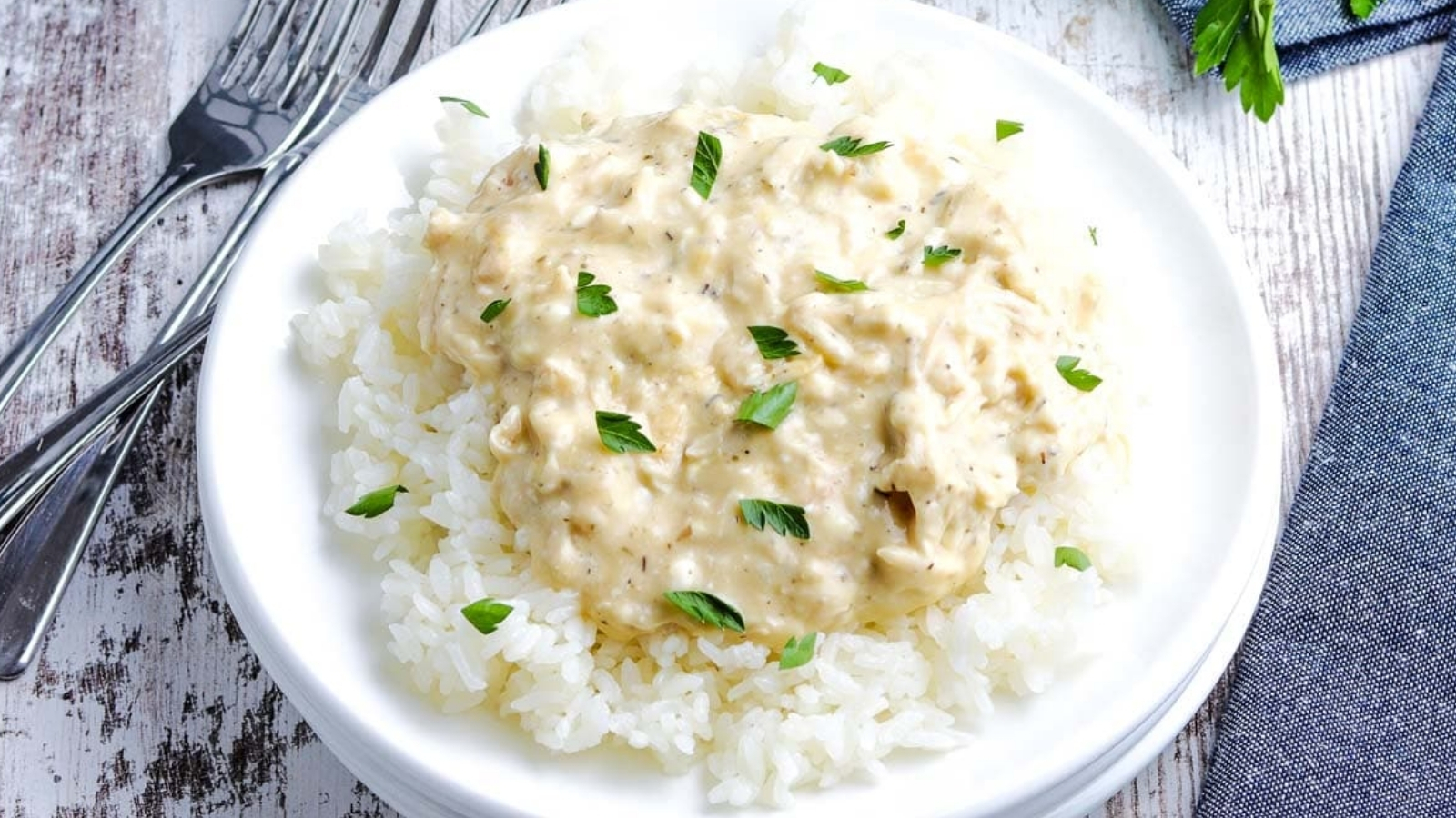 Slow Cooker Creamy Chicken on a white plate on rice topped with parsley.