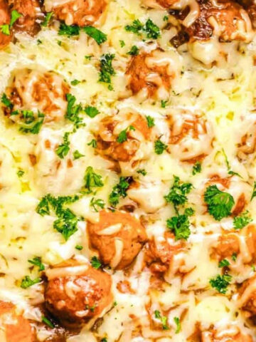 Meatballs topped with melted cheese and chopped parsley in a slow cooker.