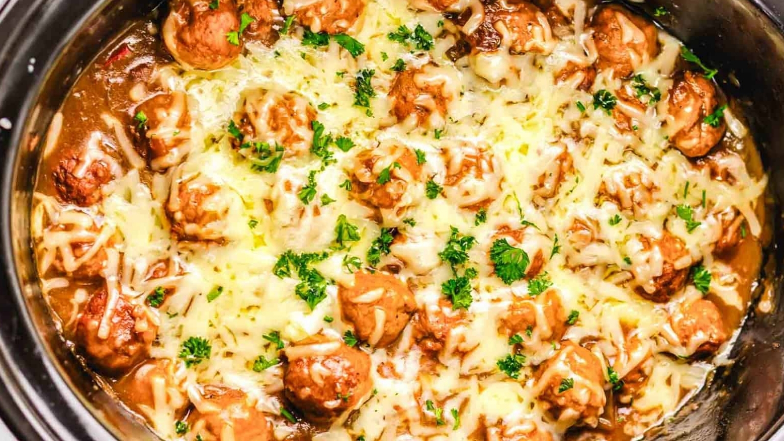 Meatballs topped with melted cheese and chopped parsley in a slow cooker.