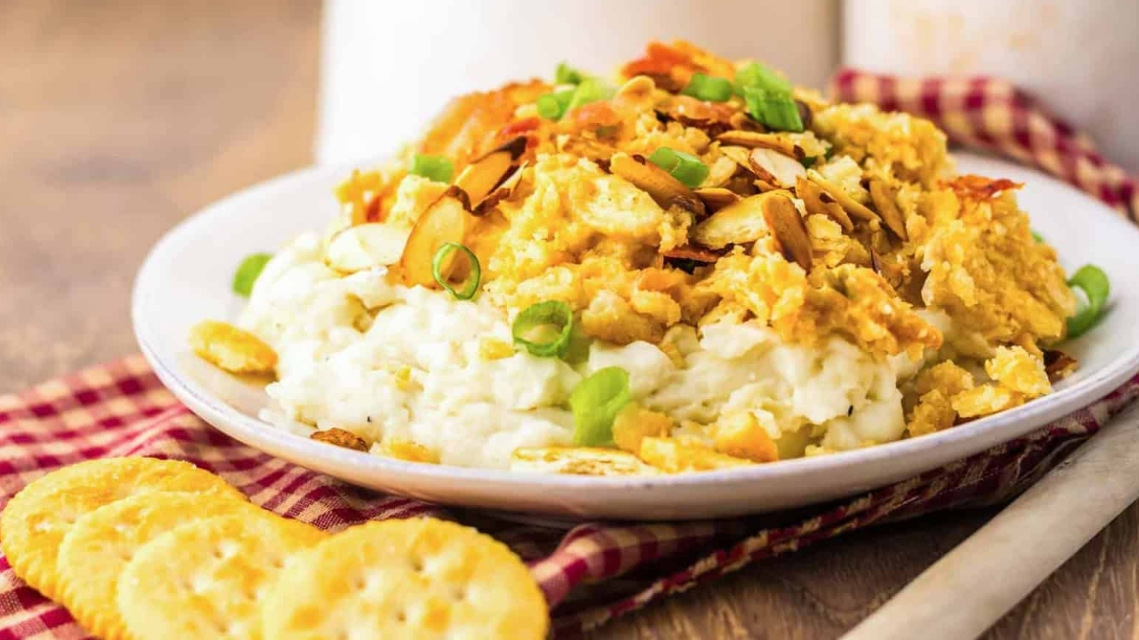 Plate of creamy chicken casserole topped with sliced almonds and green onions, served with crackers.