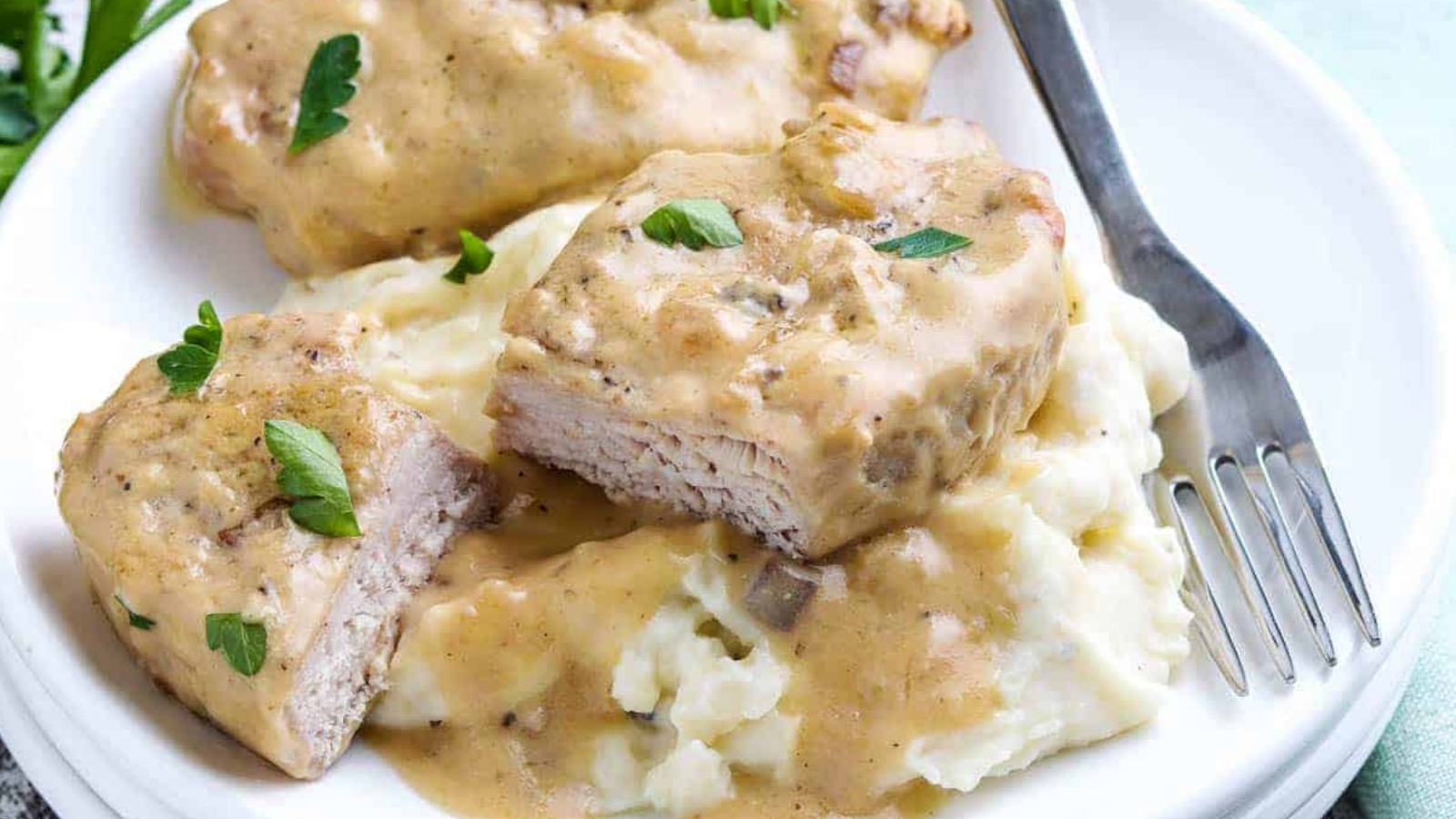 Slow Cooker Pork Chops on a plate covered with a creamy mushroom gravy and served on mashed potatoes.
