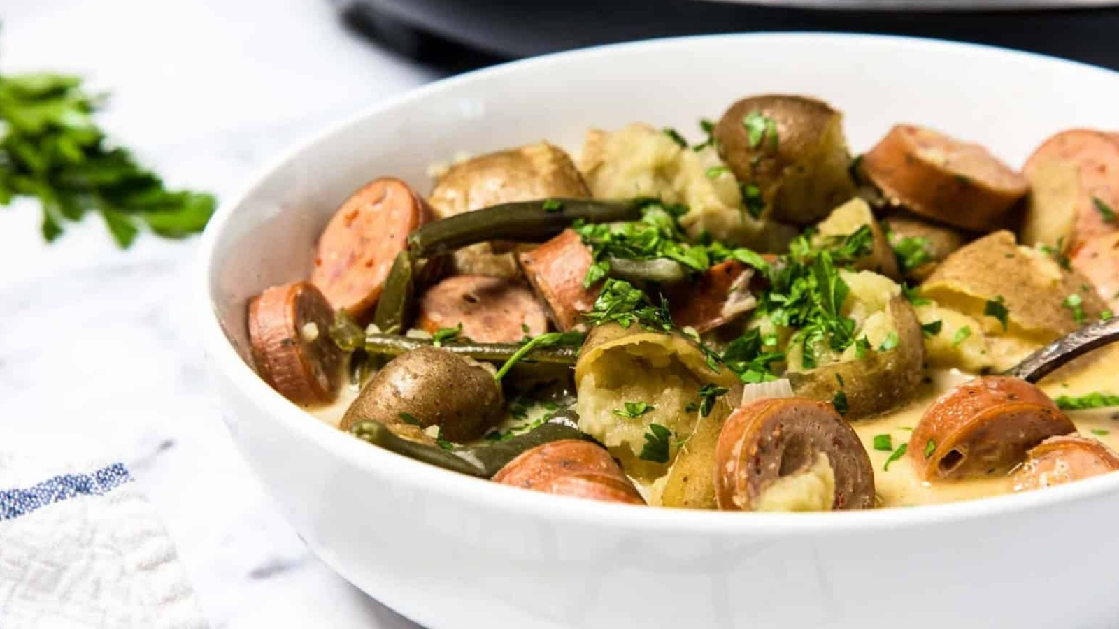 A bowl of sausage, potatoes, and green beans garnished with chopped parsley.