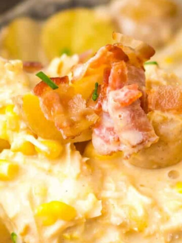 Close-up of a creamy chicken and corn chowder with chopped bacon and potatoes, garnished with fresh chives.