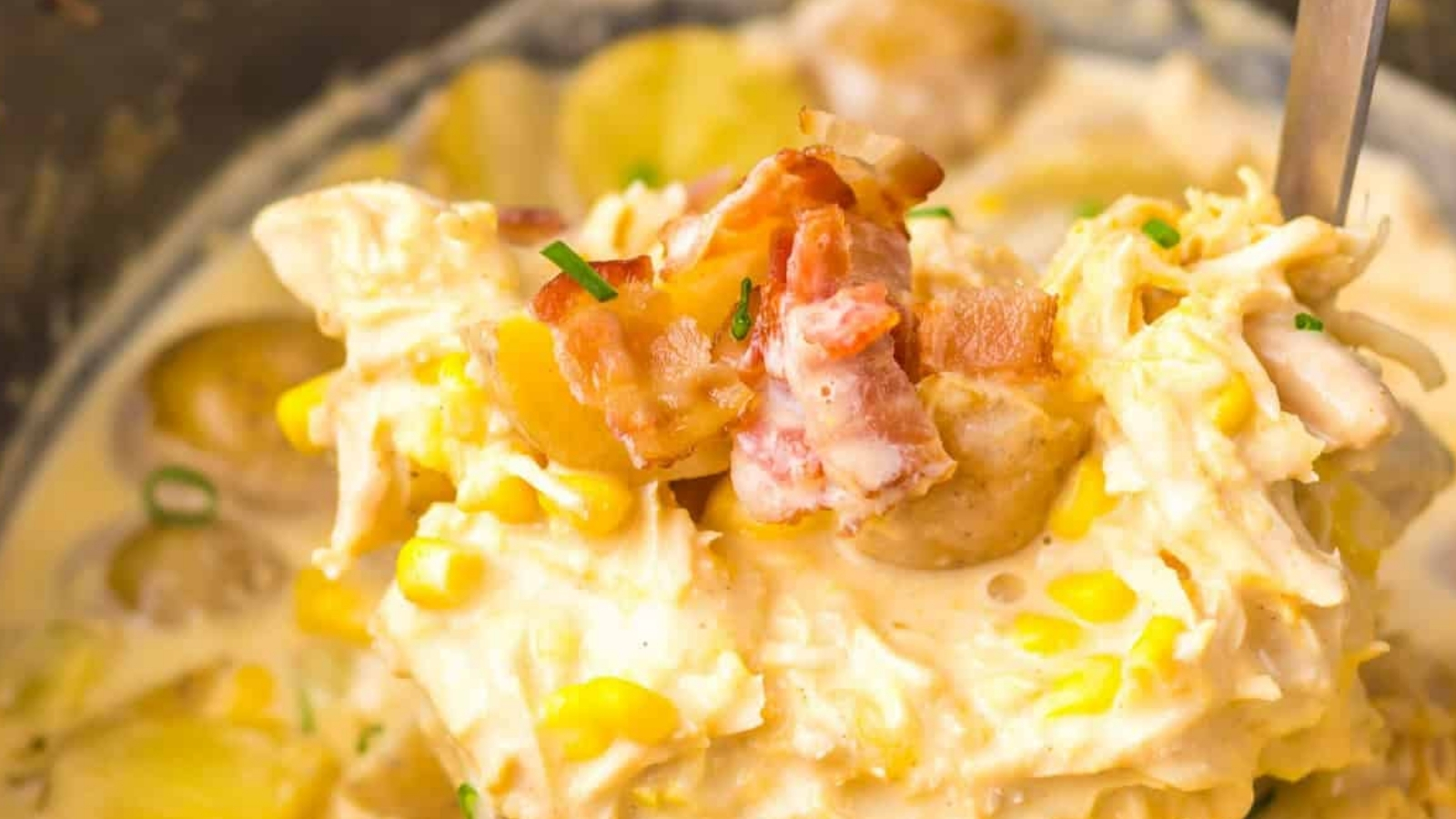 Close-up of a creamy chicken and corn chowder with chopped bacon and potatoes, garnished with fresh chives.