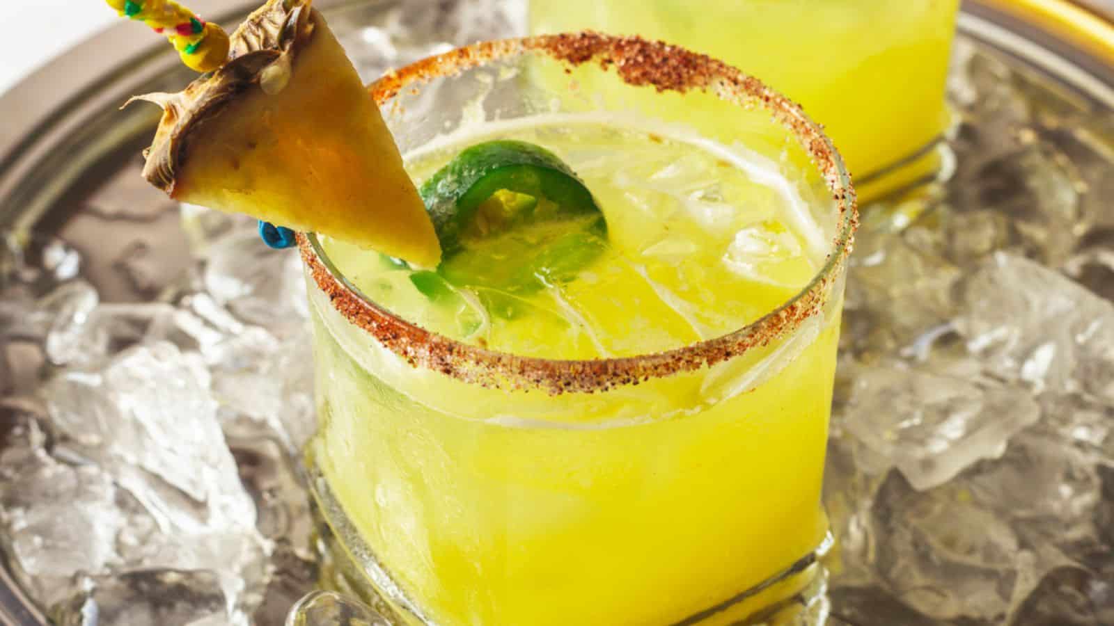 Spicy pineapple margarita mocktail served over ice in a glass with chili rim, jalapeño slice, and pineapple garnish.