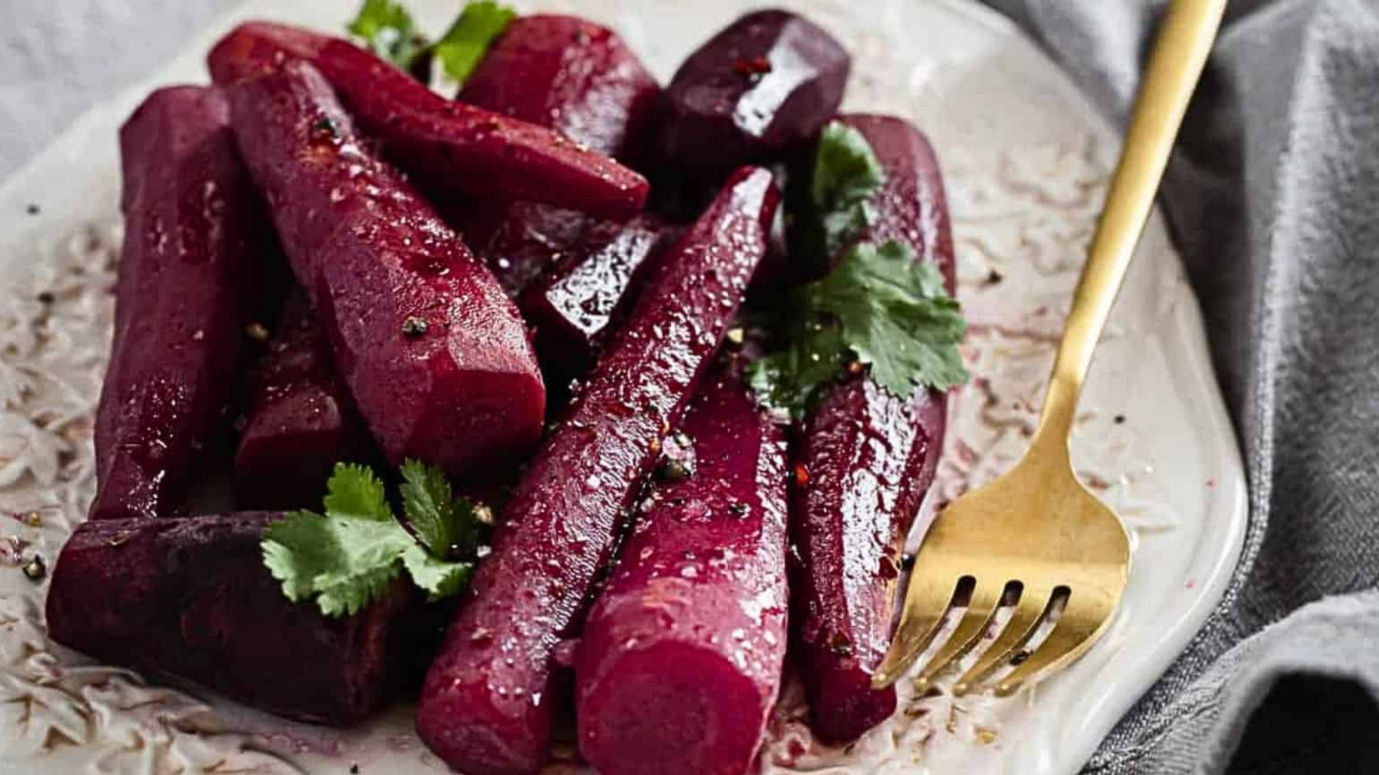 Carrots glazed in a dark red sauce piled on a patterned plate with a gold-colored fork resting beside them.