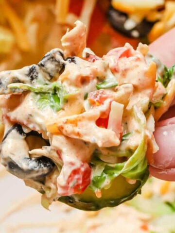 A hand holding a slice of cucumber topped with taco dip with cream cheese.