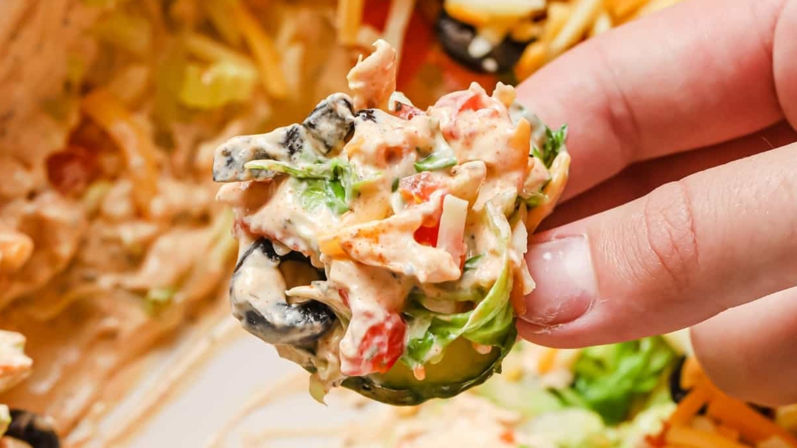 A hand holding a slice of cucumber topped with taco dip with cream cheese.