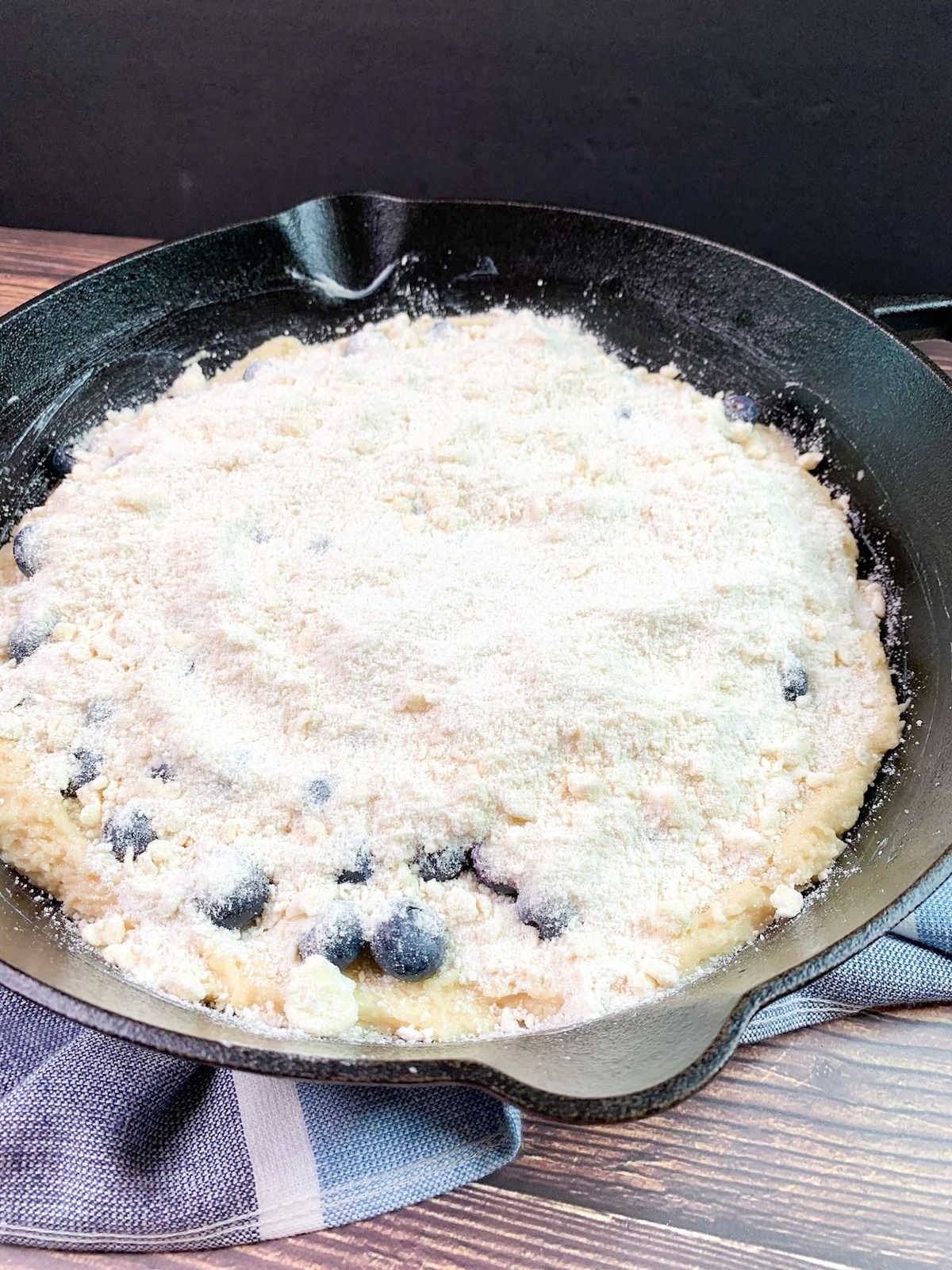 Cast iron blueberry coffee cake with crumb topping before baking.